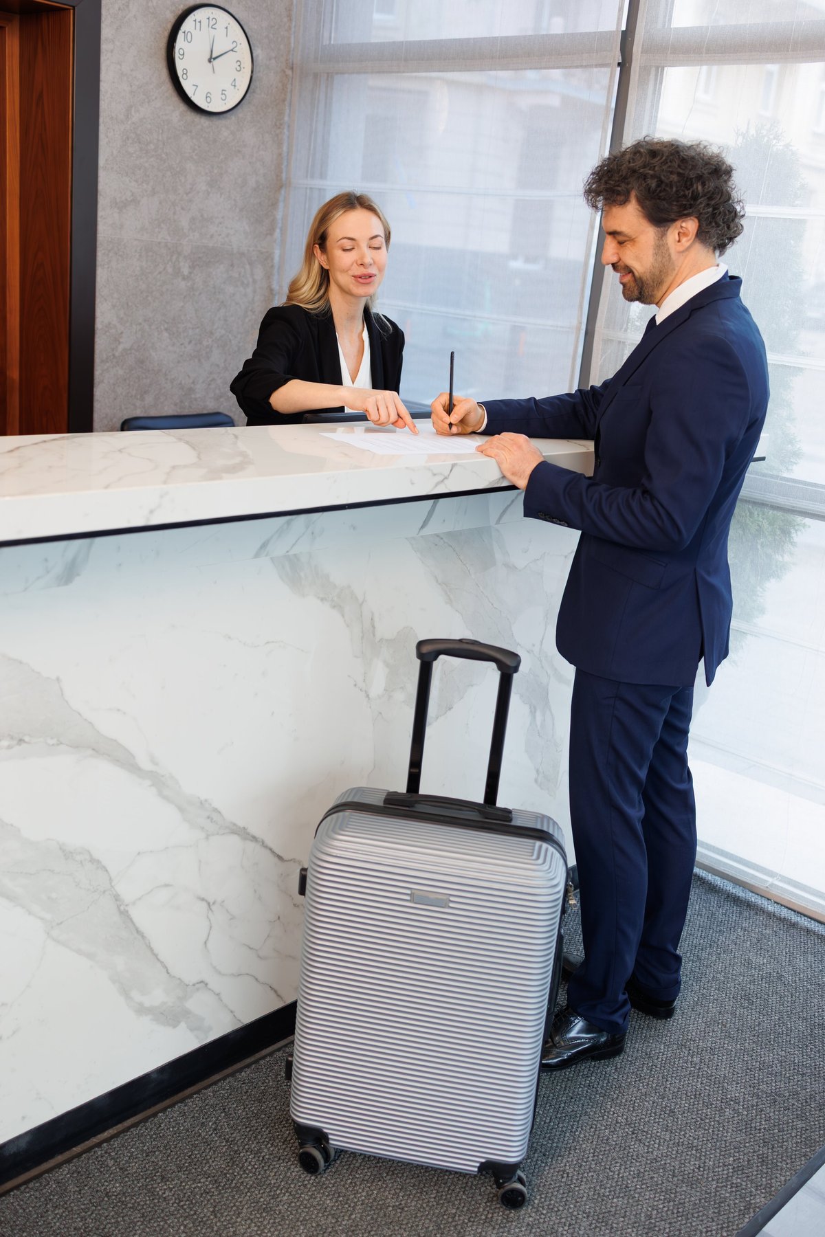 Business Guest Signing Check In Papers with Receptionist Guidance at Hotel Front Desk